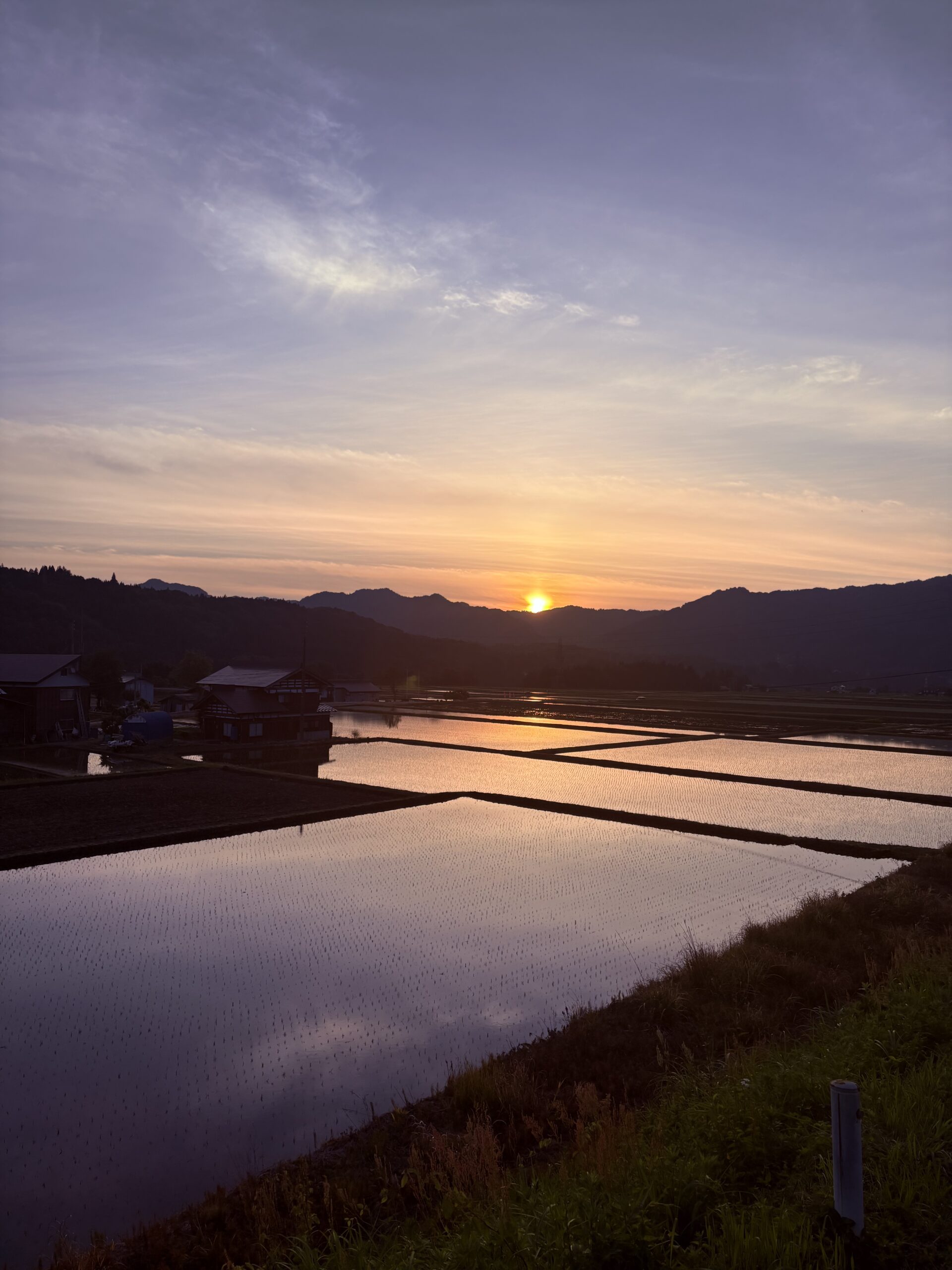 十日町の棚田に映り込む夕焼けと、山の稜線に沈むオレンジ色の夕日