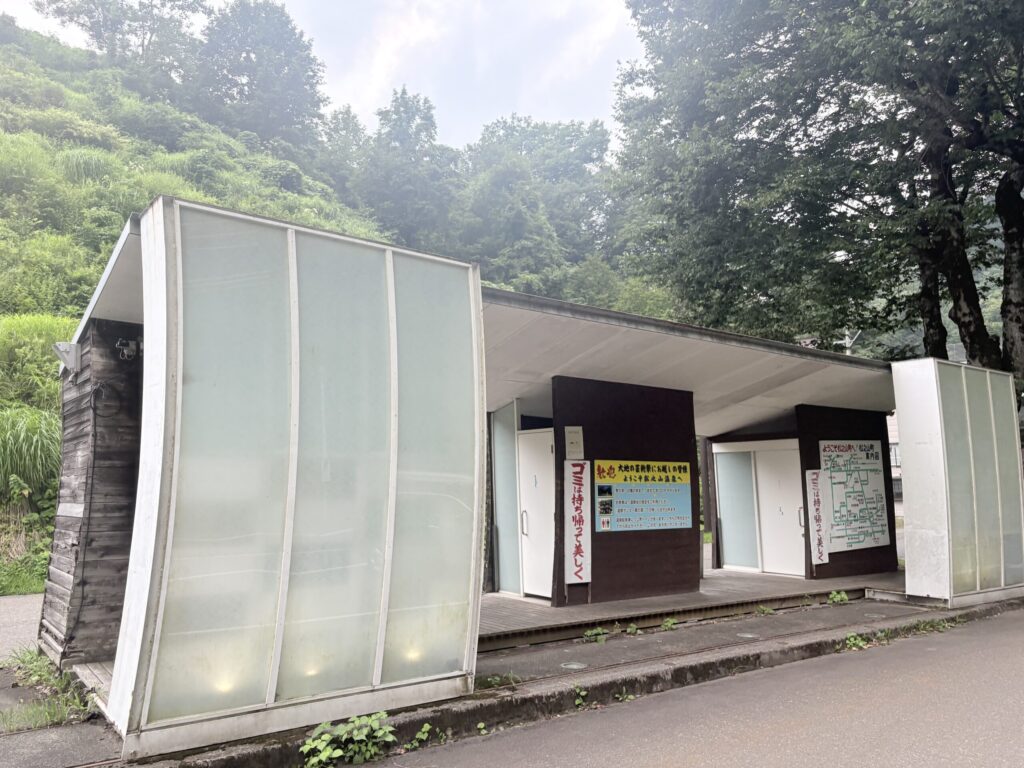 松之山温泉駐車場の公衆トイレ。乳白色のガラスパネルで覆われた建物と、松之山町の案内図が並ぶ