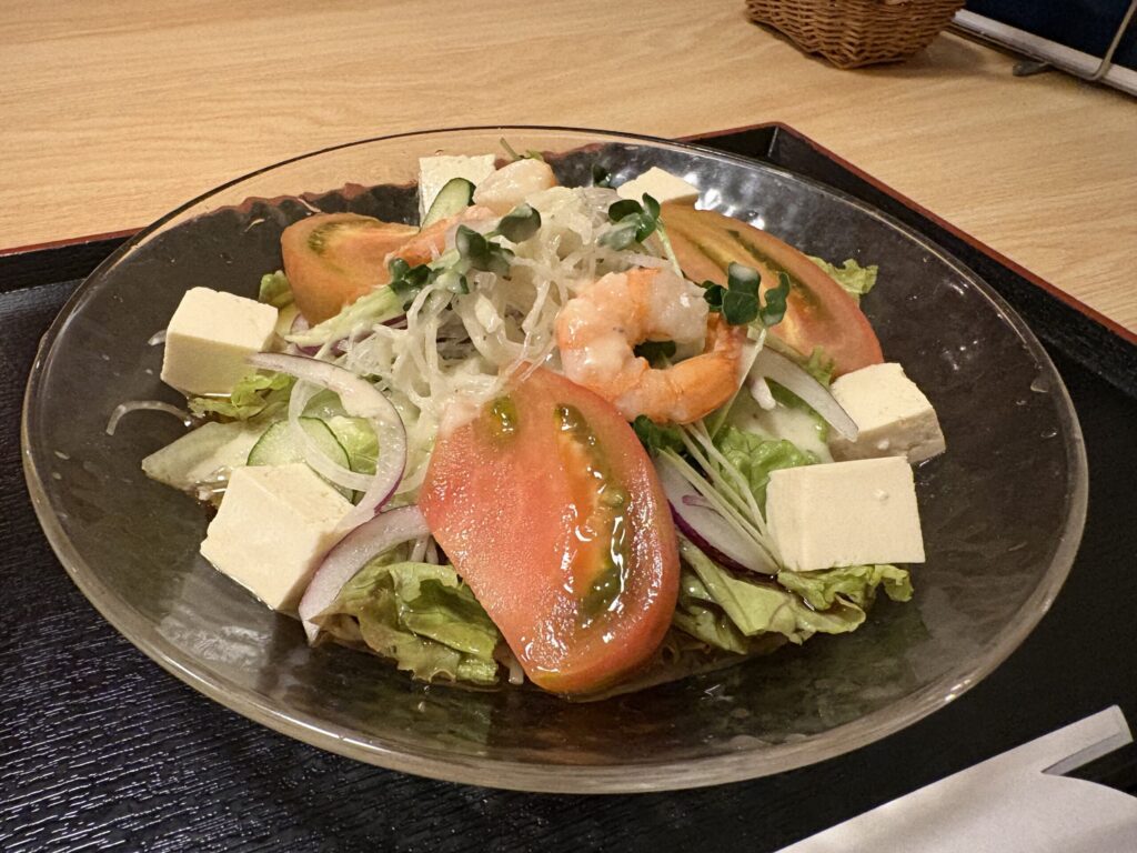 ガラス皿に盛られたサラダ蕎麦。トマト、豆腐、海老、玉ねぎのスライスが妻有そばの上にのっている