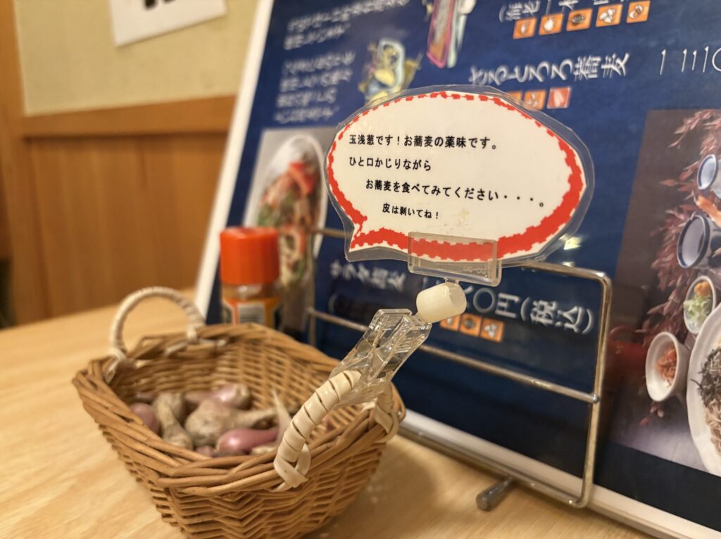 テーブルに置かれた籠入りの生の玉浅葱と、食べ方を説明した手書きの案内カード