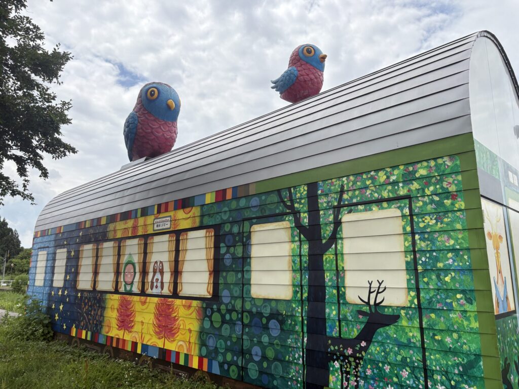 土市駅の大地の芸術祭作品Kiss&Goodbye、絵本の絵が描かれたかまぼこ型倉庫と屋根の上の2羽の鳥