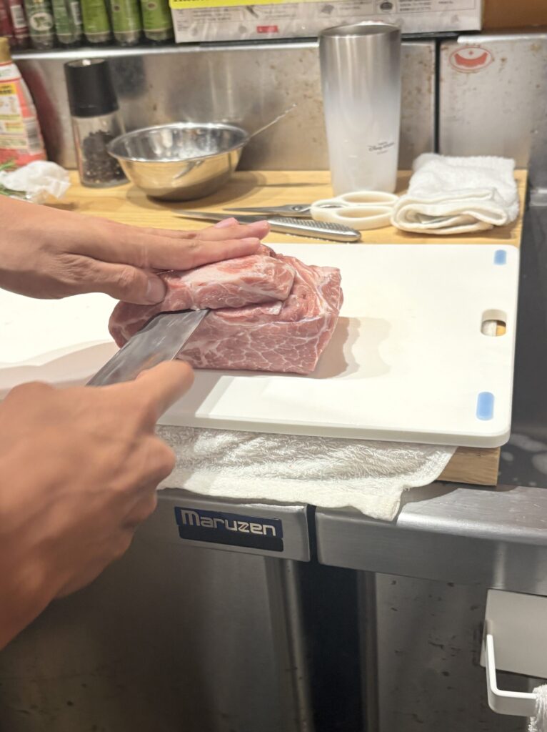 まな板の上で豚肩ロースを包丁で開くシェフの手元