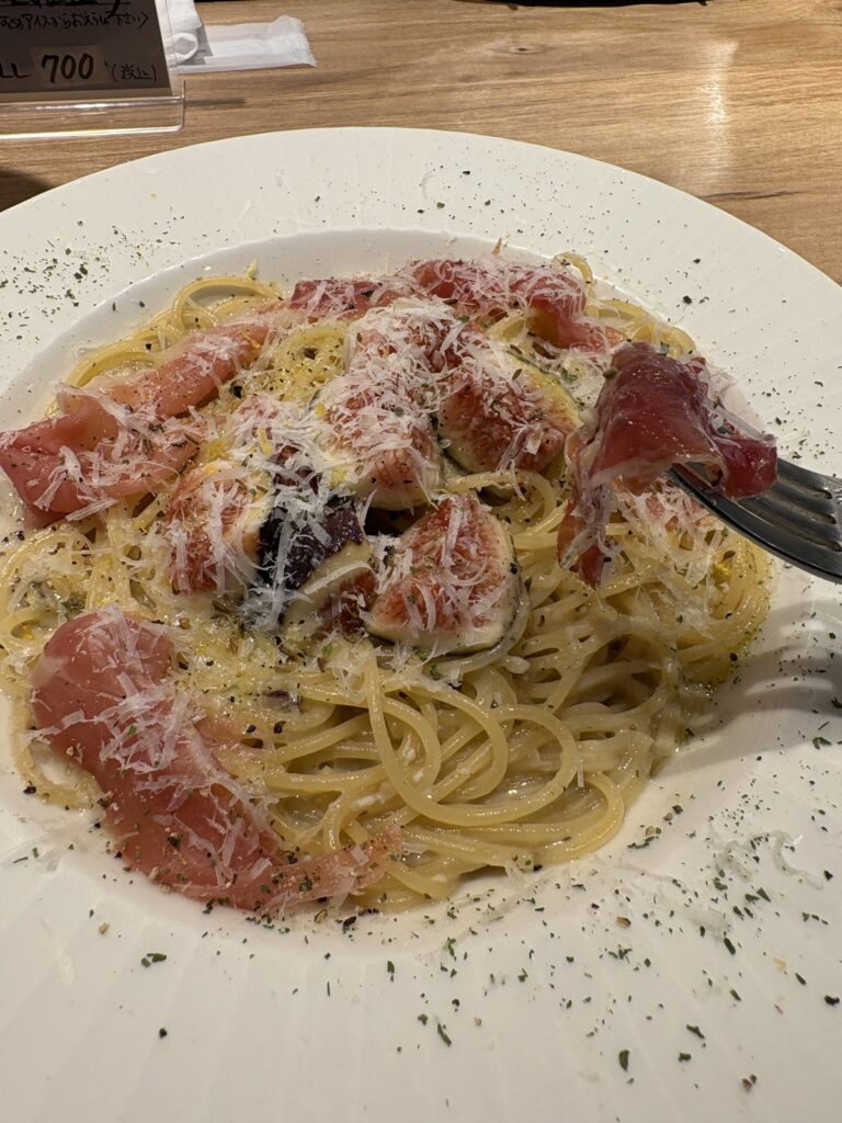 フォークで生ハムを持ち上げた黒いちじくのクリームパスタ