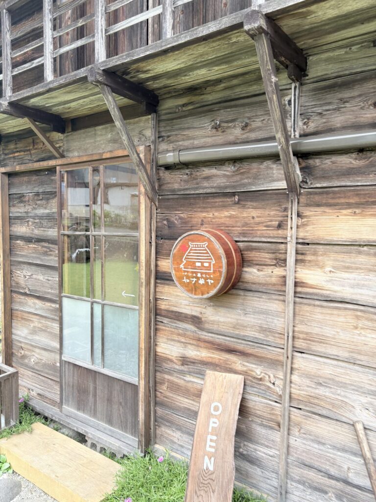 ヤナギヤの板壁に掛けられた丸い木の看板とOPENの立て看板